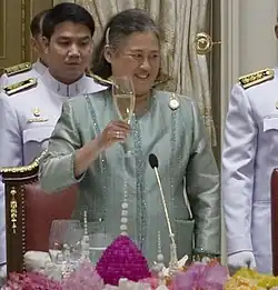 Photograph of an old lady proposing a toast with her right hand.