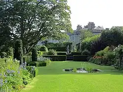 a lawn with surrounded by trees and plants, there is a large house in the background