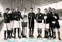 Nine men standing in an ice skating rink holding hockey sticks