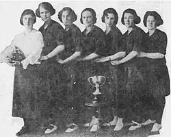 A line of seven women standing behind a large trophy