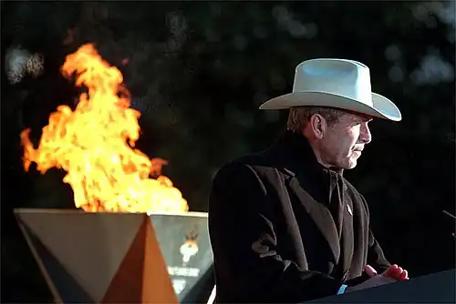 President George W. Bush, with the flame behind, speaks at the White House.