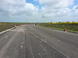 A picture of a paved, partly-complete A5758 road without any markings on its pavement and with traffic cones lining its sides
