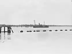 Anti-submarine boom gate in open position (foreground) and permanently anchored ship "HMAS Kinchela" (background). 1943.[gallery 13]