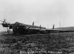 A black and white photo of a large monoplane aircraft with four propeller engines on muddy ground. The aircraft's port-side landing gear is not working, and it is lying at a steep angle with a tarpaulin over its nose.
