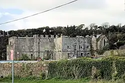 grey stone partly castellated two or three story ancient building with woods beyond