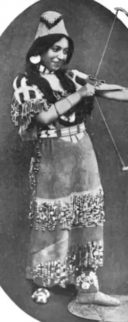 A young Cayuse woman in traditional costume, pretending to shoot an arrow