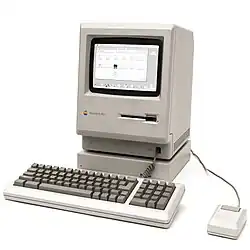 Macintosh Plus monitor, keyboard, and mouse in front of a white background