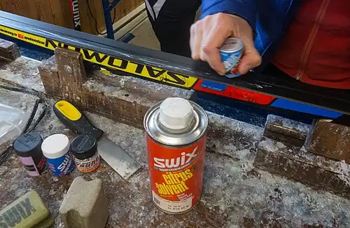 Application of grip wax to a classic cross-country ski, using a canister of wax, like those shown in the left foreground.