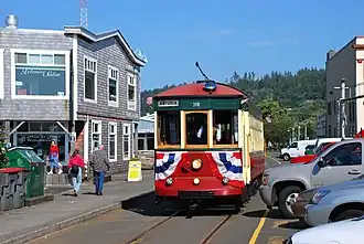 Red streetcar with creamy-white windowpanes on trolley tracks in narrow Astoria street, with green, forested hills in the background
