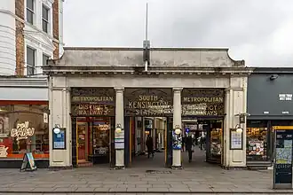 Station entrance with portico and ornamental ironwork signage above stating "Metropolitan and District Railways", "South Kensington station".
