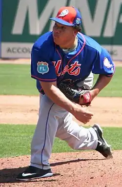 A man in a blue baseball jersey with gray pants and orange cap