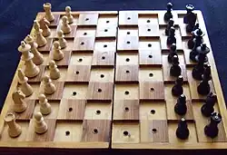 Chessboard for blind players with black pieces marked with a pin on top, black squares marked by being raised above white, and all squares having holes so the pieces can be stuck in them