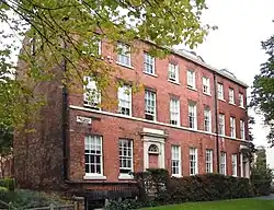 Colour photograph of Botany House consisting of a terrace of three houses. The houses are constructed of red brick with stone details and a slate roof. The whole house has three storeys and nine first-floor windows, with doorways below windows three and nine.