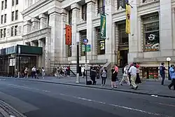 A Subway Restaurant and several stores in the building with a bus stop on the curb
