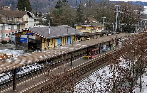 Yellow two-story building with hip roof next to double-track railway line and island platform