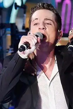 A man strikes a pose: one hand in his jeans pocket, his top two buttons undone on his dressy shirt, and the short sleeves rolled back.