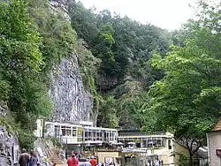 Exposed limestone cliffs with vegetation above white buildings with large windows.