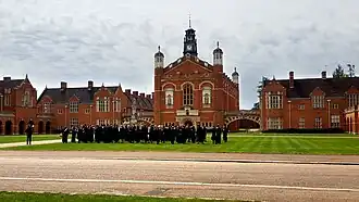 Uniformed pupils assembled on the grass amid red brick school buildings