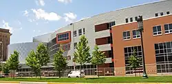 Four story brick and steel building before blue sky and clouds with trees and grass in foreground