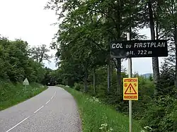 Tree-lined summit of a road with a sign post reading "Col du Firstplan, alt. 722m"