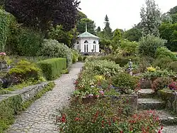an octagonal gazebo in a woodland garden with stone paths