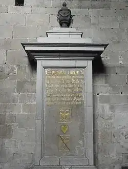 Photographie d'une plaque tombale gravée fixée contre le mur par un socle maçonné