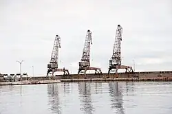 Three port cranes lined along the shore