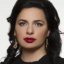 Ignatova, with black hair and dark red lipstick, against a white background, with a neutral expression.