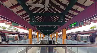 A photograph of Chinese Garden's under roof, featuring red and green beams. There are two trains at the platform