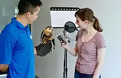 Actress recording podcast in microphone with Earth Rangers handler holding a bird to record vocals