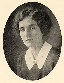A yearbook photograph of a young white woman with short curly hair, wearing a dark garment with a white collar