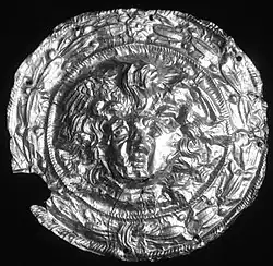 Black and white photograph of a circular gold disc with Medusa's head and hair in the centre