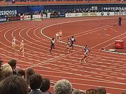 Photo of eight runners on a red athletics track with the heads of spectators in the foreground