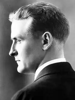 Photograph of F. Scott Fitzgerald in profile circa 1927. His back is towards the camera, and his face is in left profile. He is wearing a dark suit and white shirt. His face has a serious expression as if staring intensely at someone off-camera.
