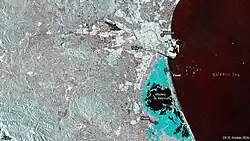 A processed image. On the left (west) the land, on the right (east) the sea in very dark red labeled "Balearic Sea". On top of the middle, a white area labeled "Valencia", surrounded to the south by a cyan line labeled "Turia". Under the middle a roundish black shape labeled "Albufera de València". Between Turia and Albufera a cyan triangle almost as big as Albufera labeled "Flood". To the south of Albufera a cyan area with black patches as big as Albufera labeled "Flood". On the right below corner a label reads "19-31 October 2024".