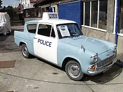 Ford Anglia car in pale blue paint, with white overpainted doors and roof. The roof also carries a Police lightbox sign and flashing blue light.