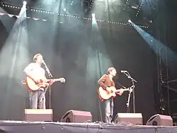 Two men playing acoustic guitar on stage in concert.