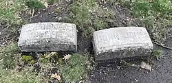 Two simple oblong gravestones on grass - the left reads "Grandma Jonesie" and the right reads "John Jones", both in sans-serif font