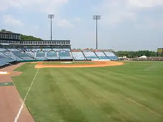 A view from the right-field line of the seating bowl at Greer. Blue seats stretch from the right-field wall, behind home plate, and beyond the third base dugout.