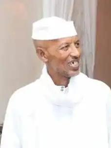 Headshot of a smiling Hassan Isse Jama dressed in white clothing looking to the right in an indoor environment