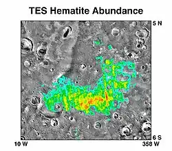 A grayscale map of an area on Mars (from 5° N to 6° S and from 10° W to 358° W (or 2° E), crossing 0° in both axes), with a false-color overlay (cyan, green, yellow, red) showing hematite abundance on the surface.