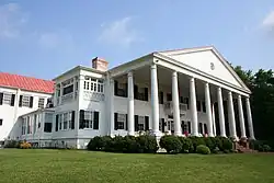 A two-story white house with red roof and columned porch.