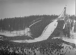 A view of a ski jump hill with crowds surrounding the landing area