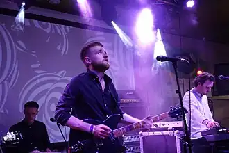 Three band members playing under purple lights