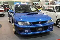 Subaru Impreza 22B-STI Version, a high-performance variant of the standard Subaru Impreza coupe. This photo shows the front of the car, which is blue with gold-colored wheels and a pink Subaru emblem.