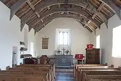 Interior of church looking towards the altar, with white walls, beamed roof and a single aisle with pews either side
