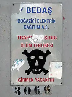 Old metal sign with black skull and crossbones and writing in red capital letters