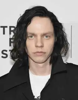 caucasian male with dark wavy long hair, piercingly gazing at the camera; background shows markings of Tribeca Film Festival