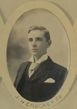 Black and white photo of a clean-shaven young man wearing a white-collar dress shirt and a black overcoat