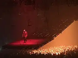 West performing on on a tilted stage floating above a crowd.